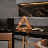 Copper finish triangular LED lamp by WOOM, sitting on a black marble table with an open book.