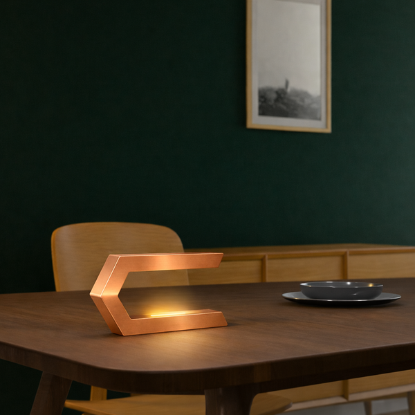 Copper finish C-shaped wooden LED lamp by WOOM with a warm glow on a dark table.