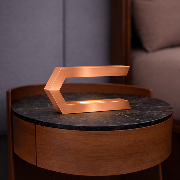 Copper finish wooden C-shaped LED lamp by WOOM, illuminating a dark green marble top on a round wooden side table.