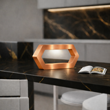 Copper finish hexagon LED lamp by WOOM on a dark marble kitchen island with an open magazine.