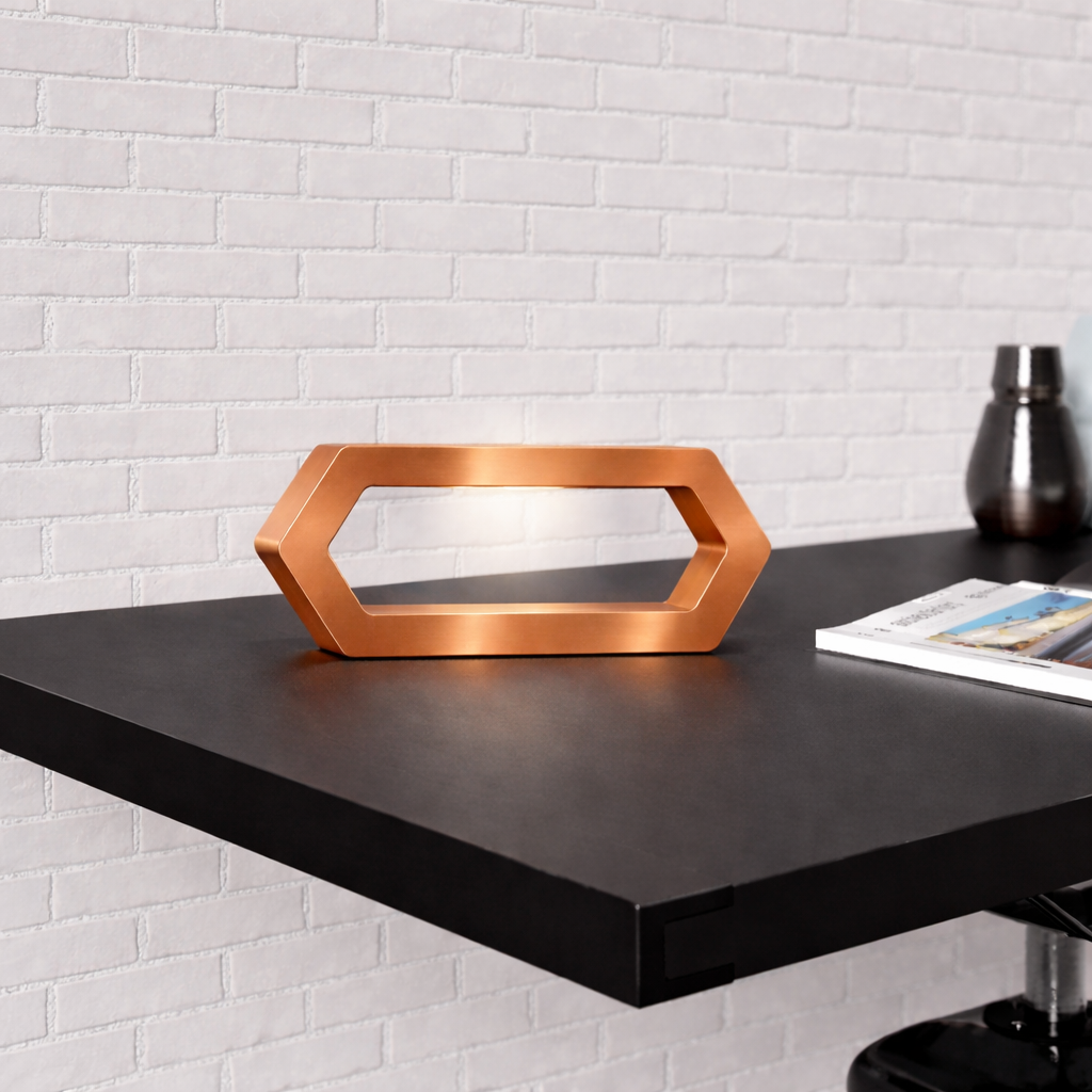 Hexagon copper finish LED lamp by WOOM on a dark desk with a magazine, against a white brick wall.