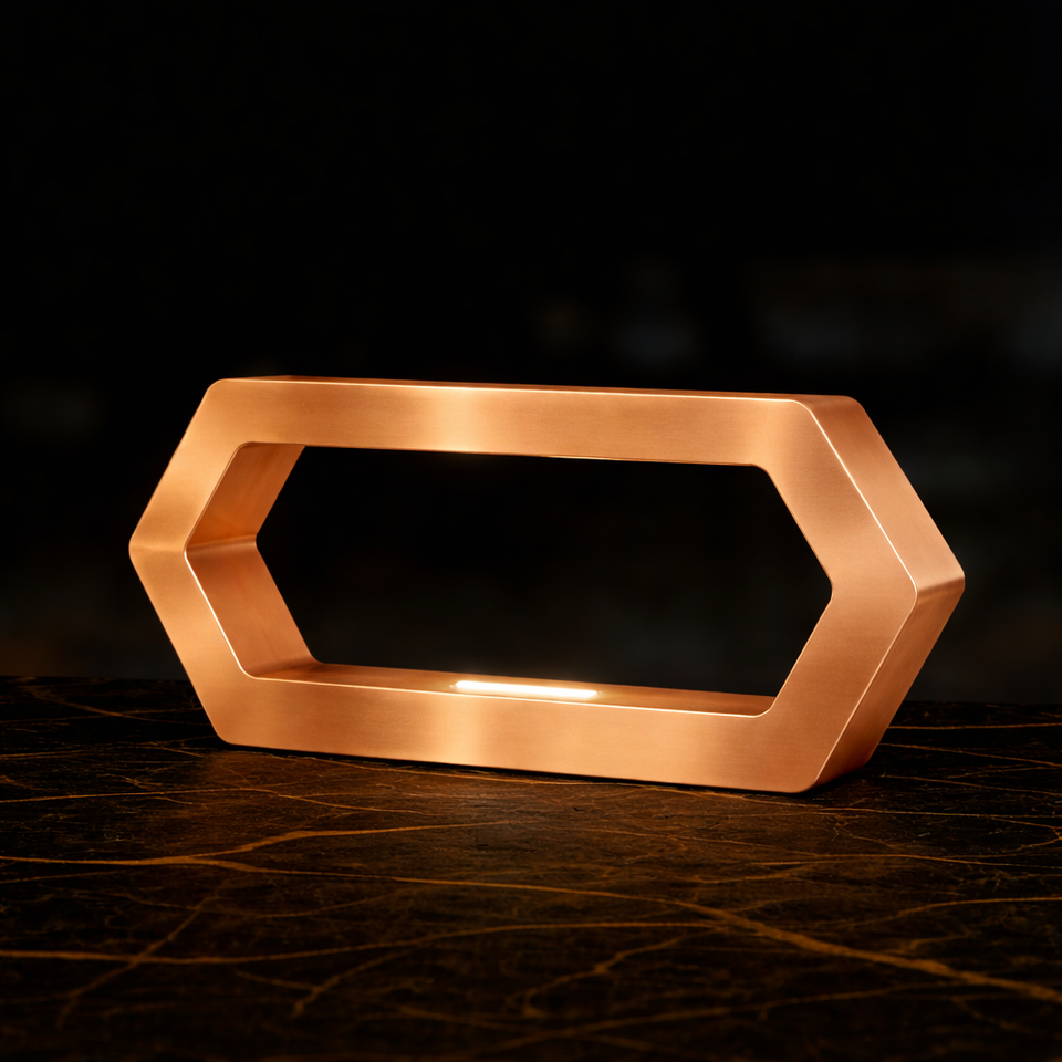 Copper finish hexagon LED lamp by WOOM with a glowing white light, sitting on a dark marbled surface.