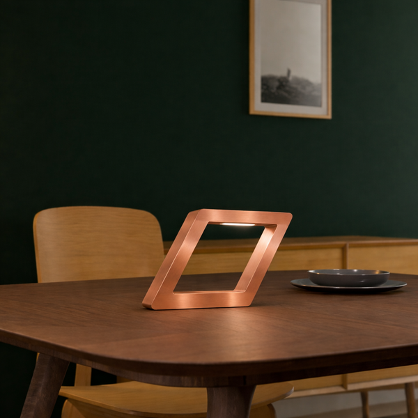 Copper finish rotatable square lamp by WOOM, with a geometric design and internal light on a dark wooden table.