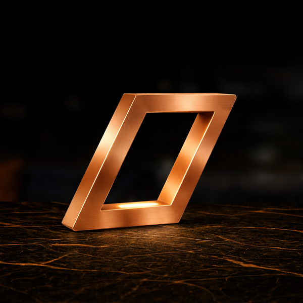 Copper finish geometric lamp by WOOM, featuring a glowing interior, on a dark marble table.