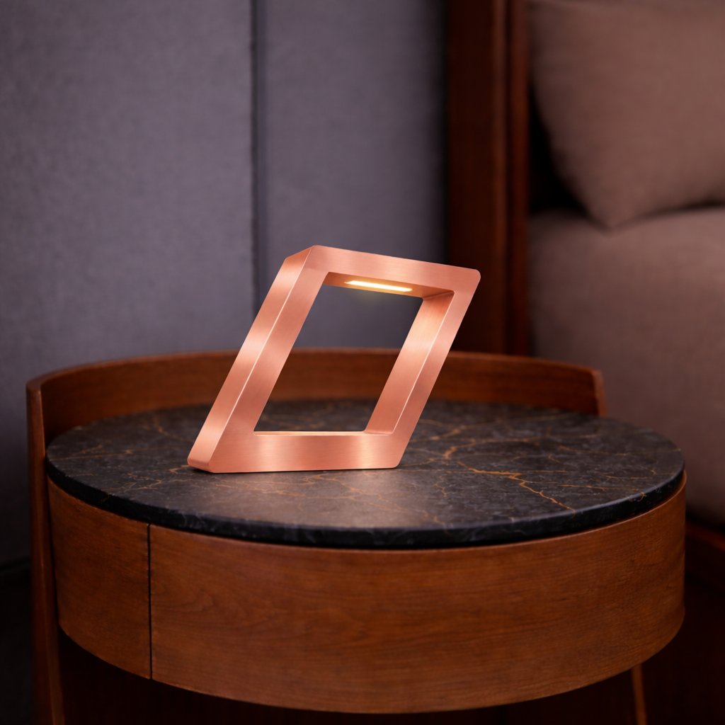 Copper finish geometric table lamp by WOOM, glowing on a dark marble-topped wooden side table.