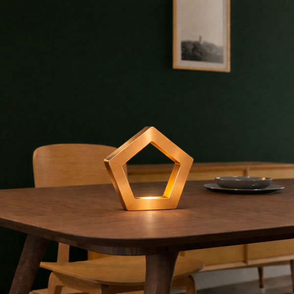 Copper finish pentagon LED lamp by WOOM, glowing warmly on a wooden dining table.