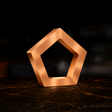 Pentagon LED lamp with a copper finish by WOOM, displaying a smooth, reflective surface on a dark patterned table.