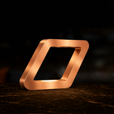 Copper-finished geometric table lamp by WOOM, with brushed texture on a dark marbled surface.