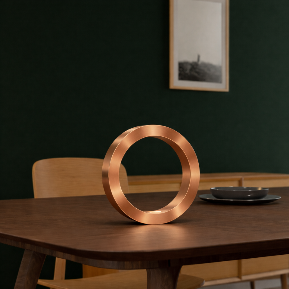 Copper finish circle lamp by WOOM standing upright on a dark wooden table.