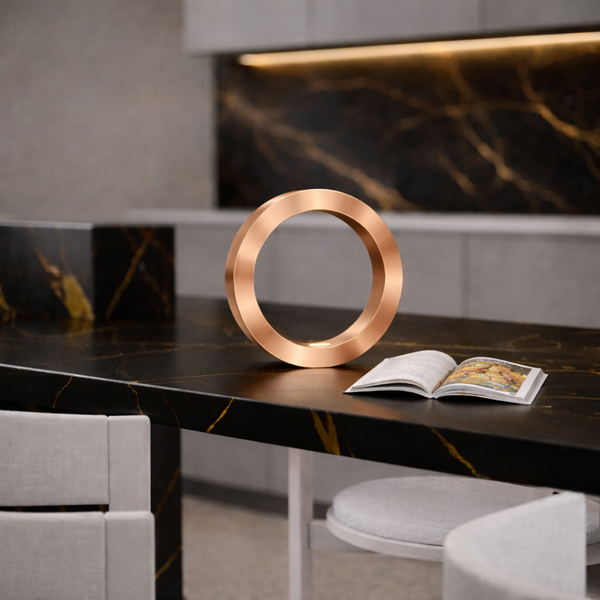 Copper finish handcrafted wooden oak rotatable circle lamp by WOOM, standing on a black marble countertop next to an open book.