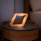 Angular copper finish table lamp by WOOM with a glowing light strip, on a round dark marble table.