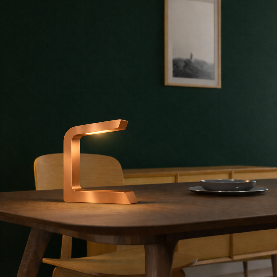 Wooden C-shaped lamp with a copper finish by WOOM, emitting warm light on a dark wooden table.