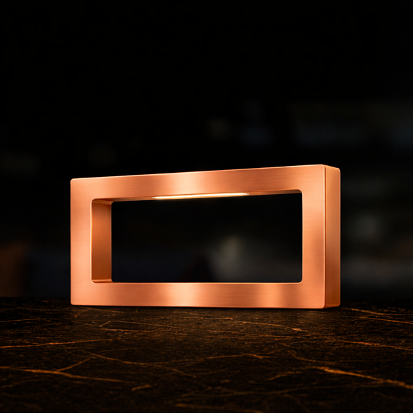 Copper-finish rectangular LED lamp by WOOM, with an internal light bar, resting on a dark patterned surface.
