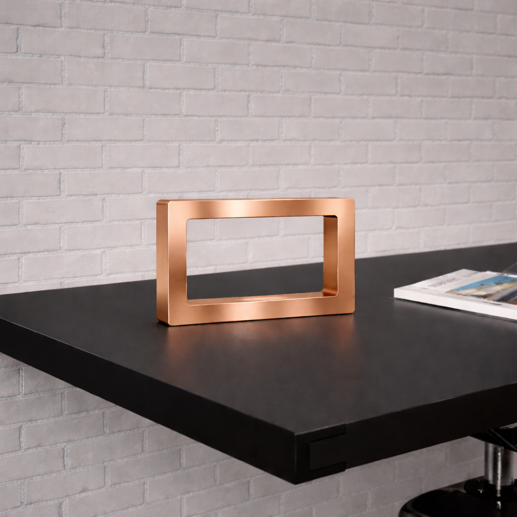 A rectangular copper-finish wooden LED lamp by WOOM, resting on a dark table against a white brick wall, with a magazine nearby.
