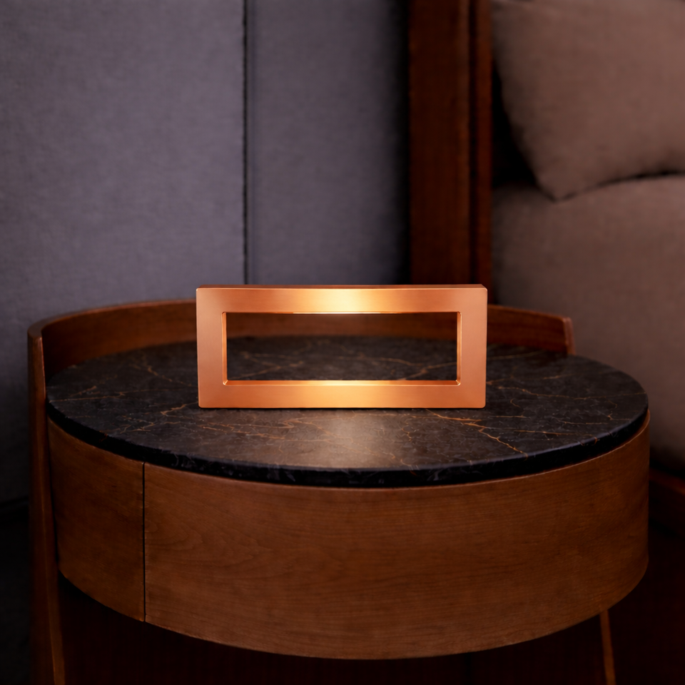 Copper finish rectangular LED lamp by WOOM, with a handcrafted oak base, on a dark marble-top table.
