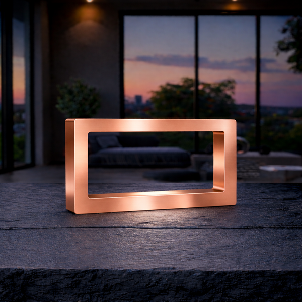 Copper finish wooden rectangular LED lamp by WOOM, casting warm light on a textured stone surface, with a sunset patio background.