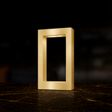 Gold finish rectangular wooden table lamp by WOOM with an internal light strip, standing on a dark marble surface.