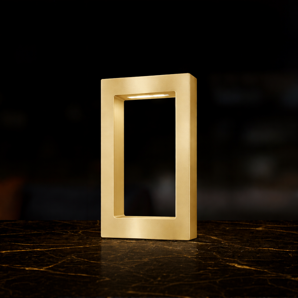 Gold finish rectangular wooden table lamp by WOOM with an internal light strip, standing on a dark marble surface.