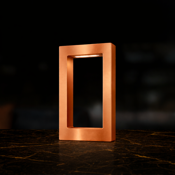 Copper finish rectangular lamp by WOOM with an illuminated interior, on a dark marble surface with gold veins.