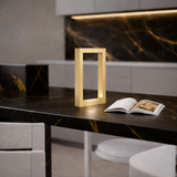 Gold rectangular wooden lamp by WOOM, illuminated on a black marble counter with gold veins, beside an open magazine.