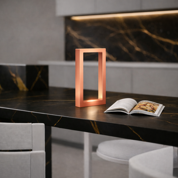 Copper Finish Rectangular Lamp by WOOM with warm glowing light on a dark marble counter.