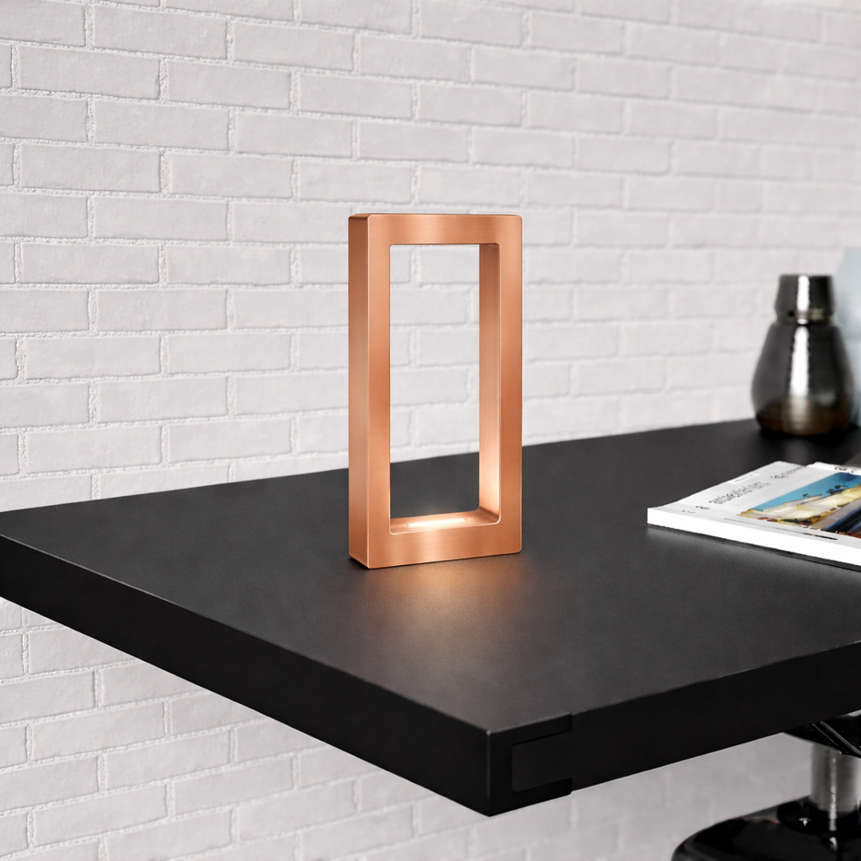 A rectangular copper finish oak table lamp by WOOM, with a warm glow on a black shelf.