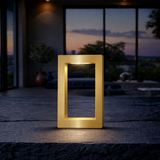 Rectangular wooden lamp with a gold finish by WOOM, emitting light on a dark stone surface.
