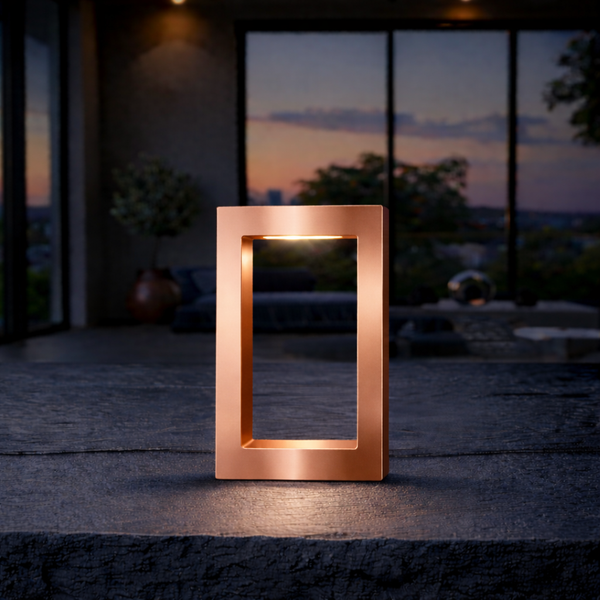 Copper finish rectangular lamp by WOOM, emitting warm light on a dark, textured surface.