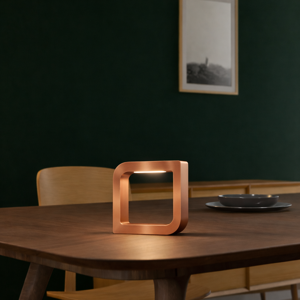 Copper finish square LED table lamp by WOOM with rounded corners on a dark wooden table.