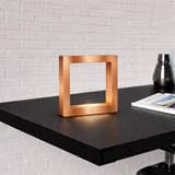 Copper finish square table lamp by WOOM with an inner light on a dark desk.