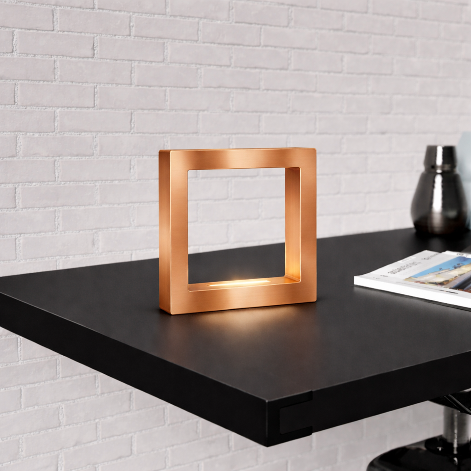 Copper finish square table lamp by WOOM with an inner light on a dark desk.