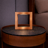 Square oak wood lamp with a copper finish by WOOM, emitting warm light onto a black marble table.