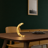 Gold finish C-curved wooden desk lamp by WOOM, illuminating a dark table.
