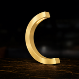 Gold finish C-curved desk lamp by WOOM, with a light strip on its inner curve, resting on a dark, textured surface.