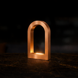 Copper finish U-shape curved desk lamp by WOOM, with internal light on a dark marble surface.