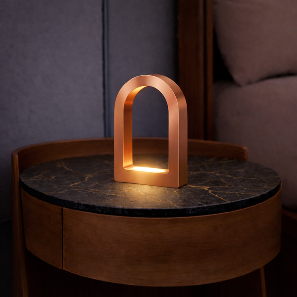 Copper finish U-shape curved desk lamp by WOOM, emitting a warm glow on a dark marble-top table.
