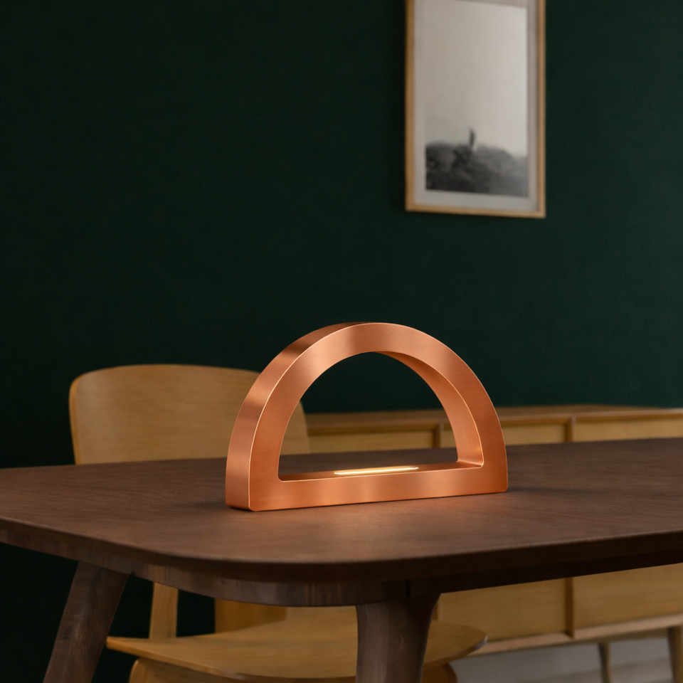 Copper finish oak arc-curved wooden desk lamp by WOOM, with an illuminated light bar, on a dark wood table.