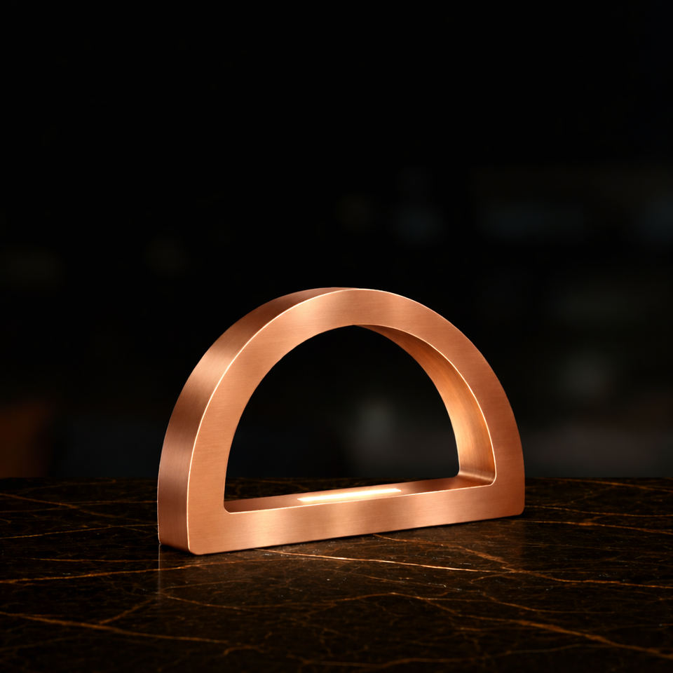 Copper finish arc-curved desk lamp by WOOM with an internal light strip, on a dark marble surface.