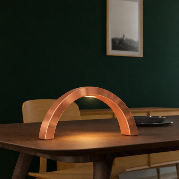 Contemporary arc-curved copper finish oak table lamp by WOOM, casting a warm glow on a wooden dining table.