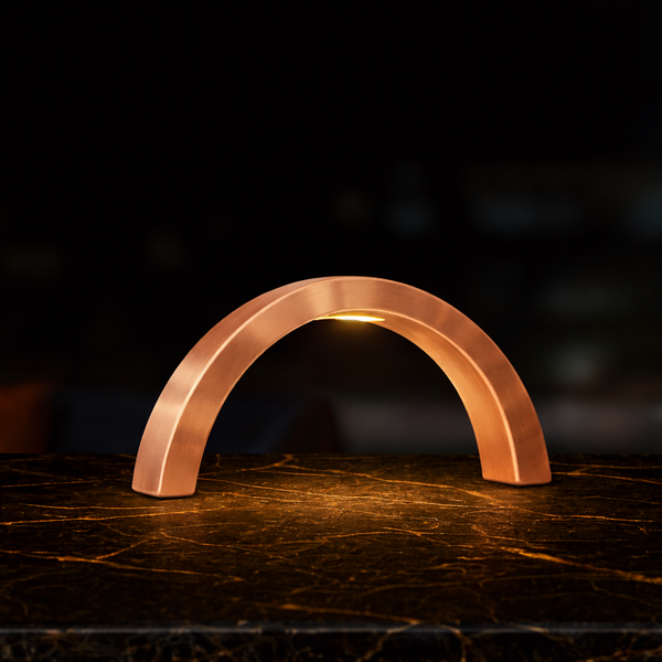 Copper finish arc-curved table lamp by WOOM, casting light onto a dark marble table.