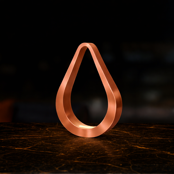 A copper finish teardrop table lamp by WOOM glowing softly on a dark, veined marble surface.