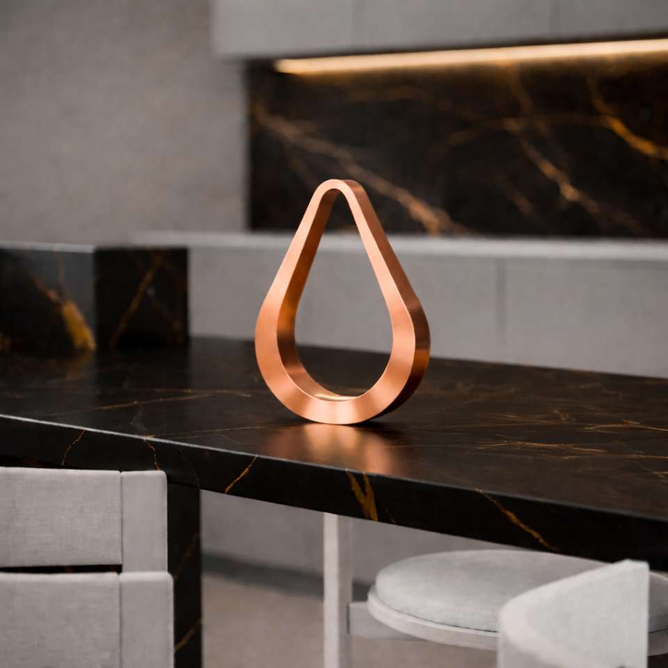 Copper-finished teardrop shaped table lamp by WOOM, a sleek decorative piece on a black marble counter.