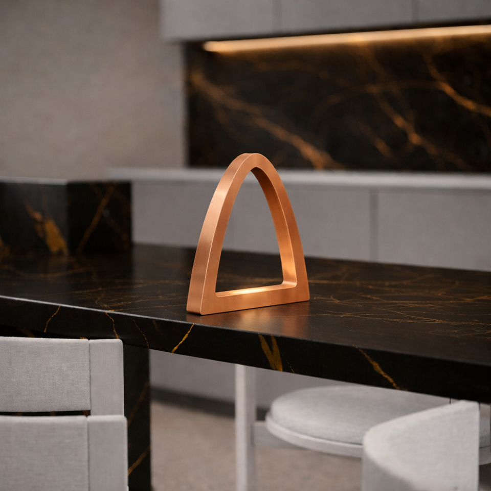 Copper finish arched desk lamp by WOOM, with a minimalist design, sitting on a black marble countertop.