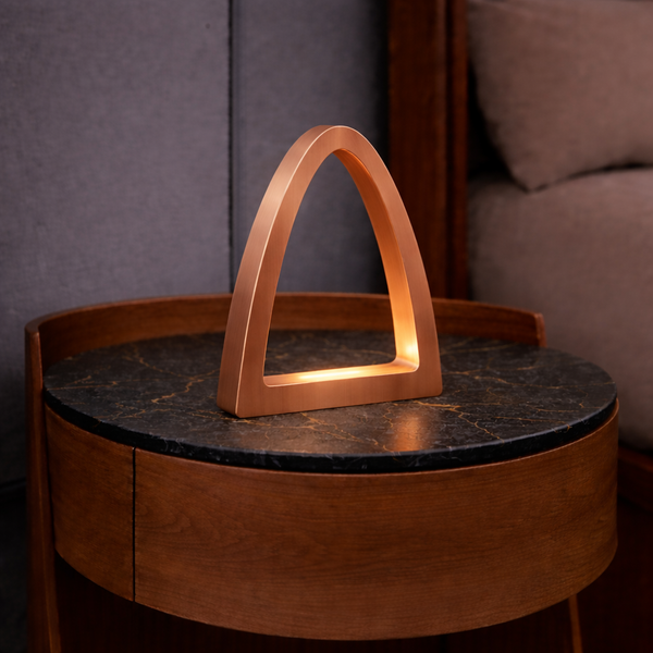 Copper finish arch-curved oak desk lamp by WOOM, casting a warm glow on a dark marble table.