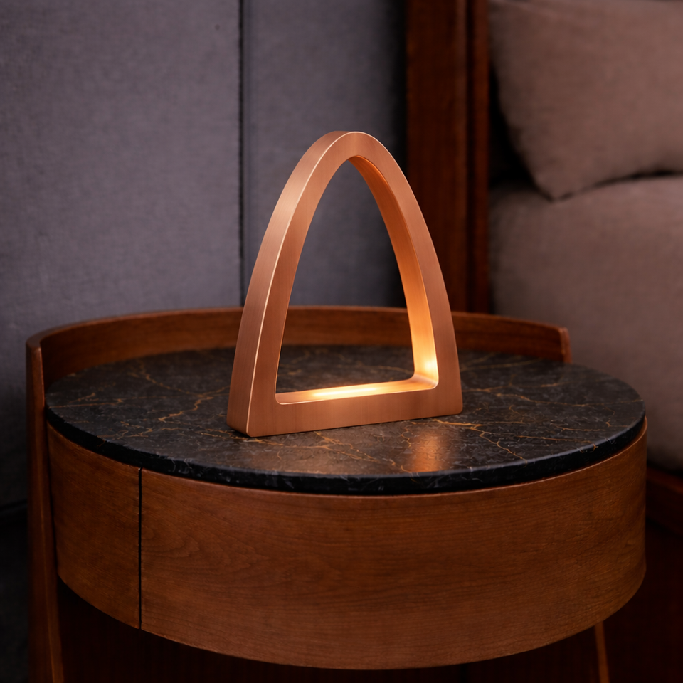 Copper finish arch-curved oak desk lamp by WOOM, casting a warm glow on a dark marble table.