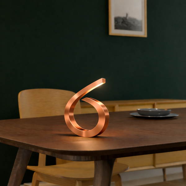 Copper-finished spiral desk lamp by WOOM with an illuminated tip, on a dark wooden table.