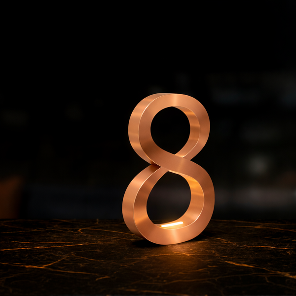 Copper finish infinity shaped lamp by WOOM on a dark marbled surface with golden veins.