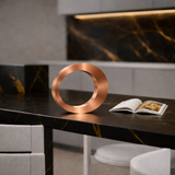 Copper finish wooden lamp by WOOM, oval-shaped, standing on a dark kitchen counter with an open cookbook.
