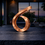Copper-finished spiral table lamp by WOOM, with an illuminated tip, on a textured dark surface.