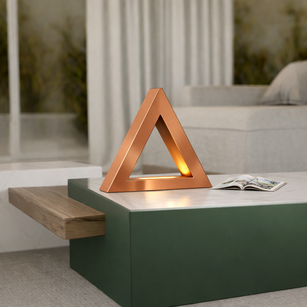 Copper finish handcrafted oak triangular lamp by WOOM, emitting a warm glow on a white marble coffee table.